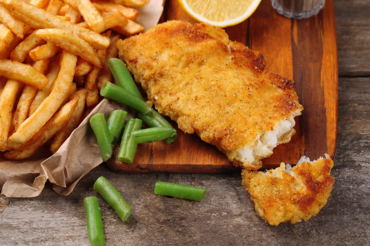 Filetti di branzino croccanti - Breaded fried fish fillet and potatoes with asparagus and lemon on cutting board and rustic wooden background