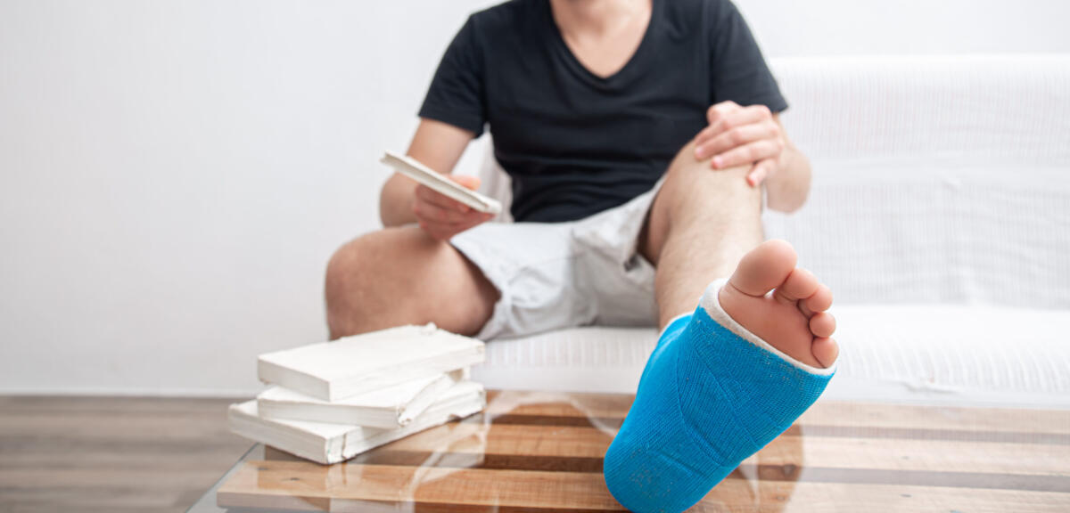 La magnetoterapia con campi elettromagnetici pulsati - Man with broken leg in blue splint for treatment of injuries from ankle sprain reading books at the home rehabilitation.