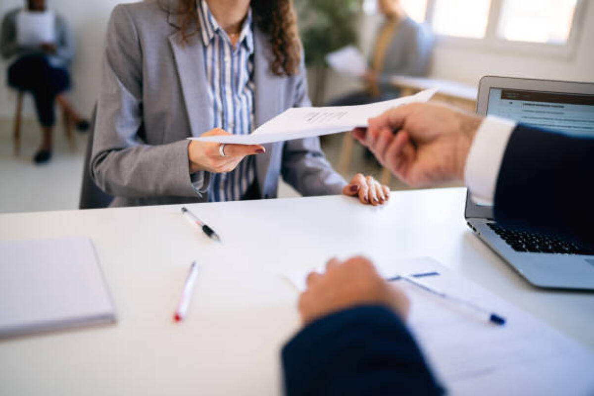 Manovra finanziaria 2026: 4 imprese su 5 non conoscono gli incentivi sul costo del lavoro - In the office young Caucasian female candidate, giving her CV or application form to male recruiter during a job interview 
Other candidates sit on the chair and wait for their turn